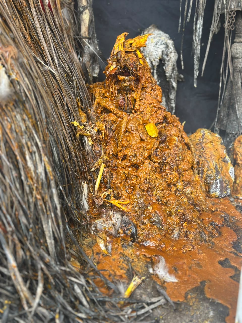 A shrine mound thick with palm oil, standing among the emblems